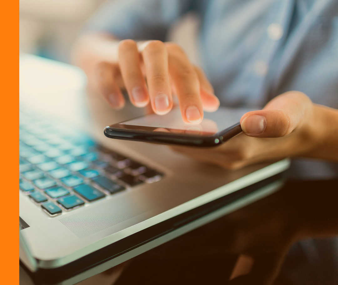 HAUTWENDE: Selbsttests Nahaufnahme einer Person, die vor einem Laptop sitzt und ein Smartphone in der Hand hält.